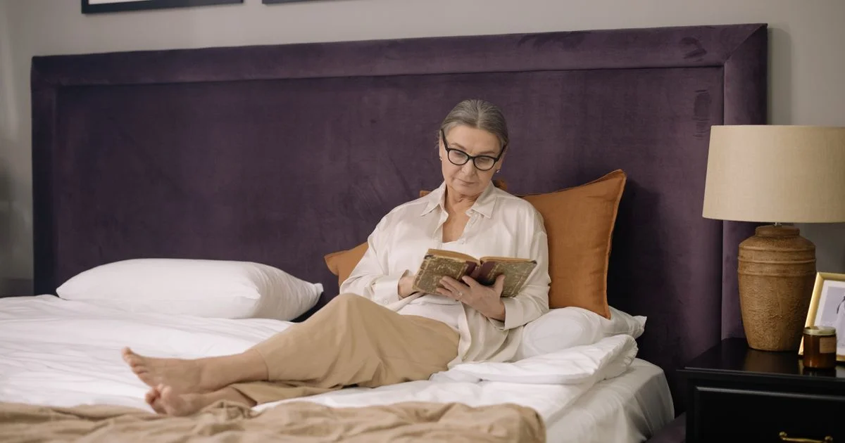 Older woman sitting upright in bed reading, the position an adjustable bed base is bought for