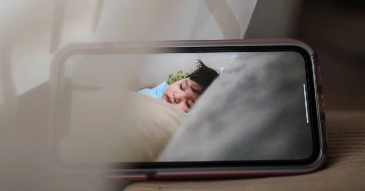 A video feed of a sleeping child on a phone screen, the app half of an affordable smart baby monitor