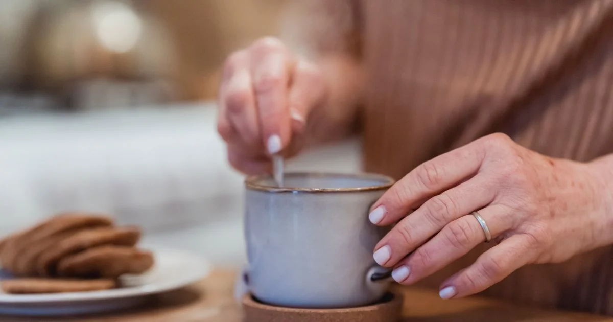 Hands stirring a hot drink in a ceramic mug on a coaster, the everyday moment behind asking are mug warmers worth it