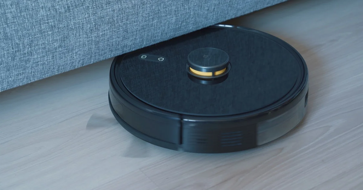 Best budget robot vacuums for hardwood floors, shown cleaning under a sofa on a wood floor