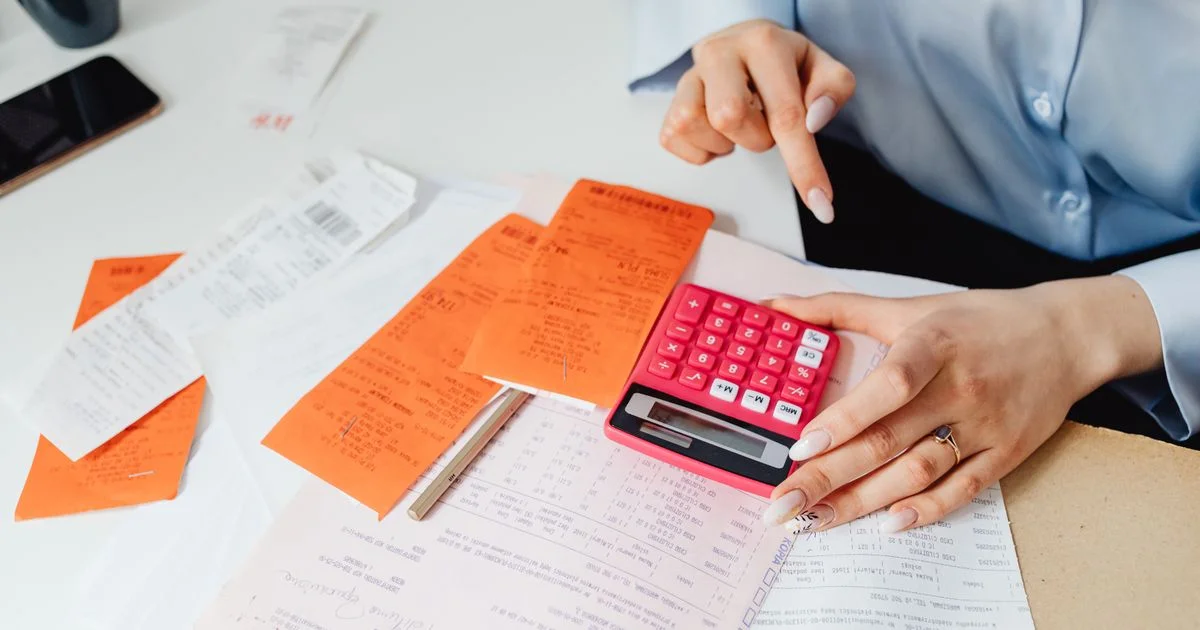 Pile of paper receipts, a calculator and a phone on a desk, the manual work a good expense report app replaces
