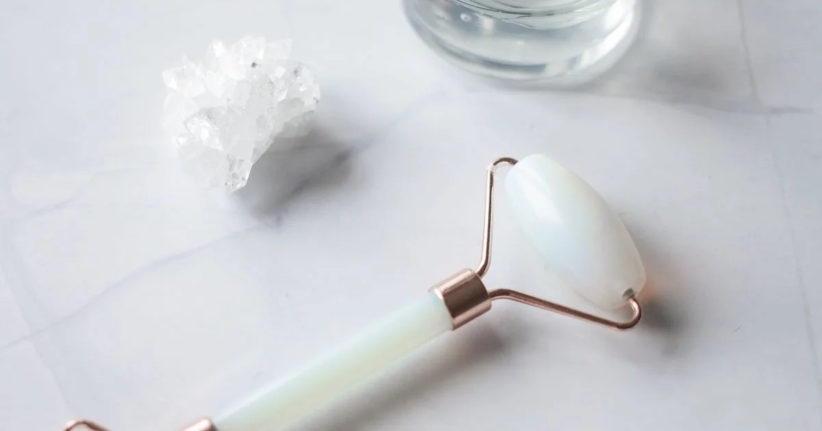 Jade roller and gua sha stone, examples of a face sculpting tool, laid on a marble counter
