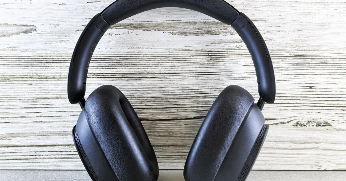 Black over-ear headphones on pale wood with both ear cushions in view, the kind of pair a budget AirPods Max search is aimed at