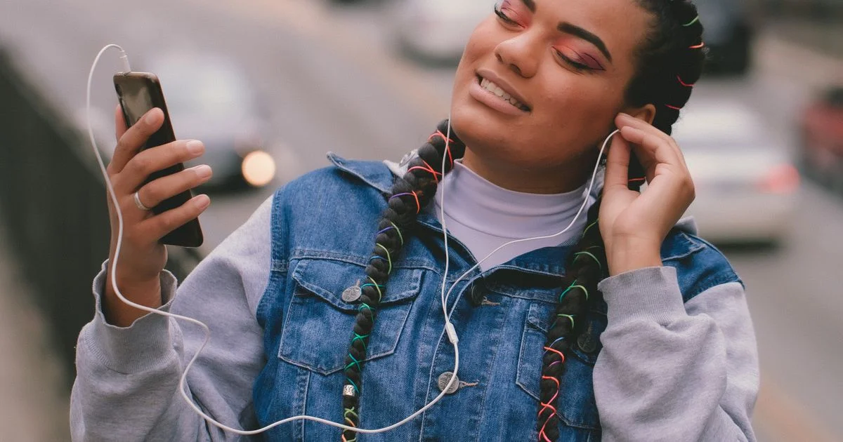 A woman listening through earbuds while holding her phone on a street, the commute where a cheap language learning app under $10/month actually gets used