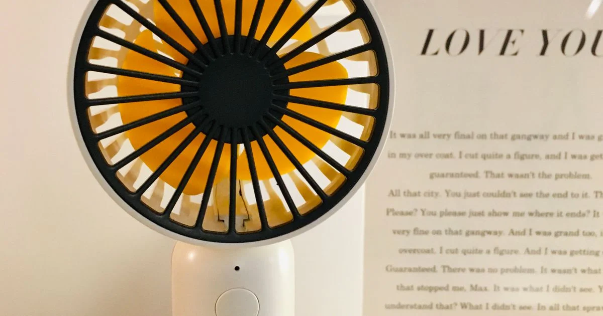 A small handheld portable fan on a desk, the tier above a cheap portable neck fan
