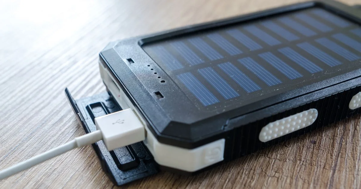 A cheap solar power bank on a wooden table with its small built-in solar panel and USB port flap open