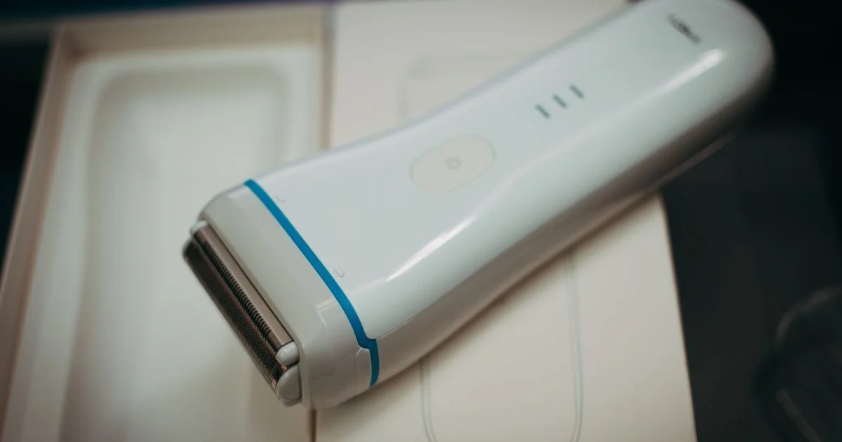 A white cordless electric razor for women with a gold foil head resting on its packaging