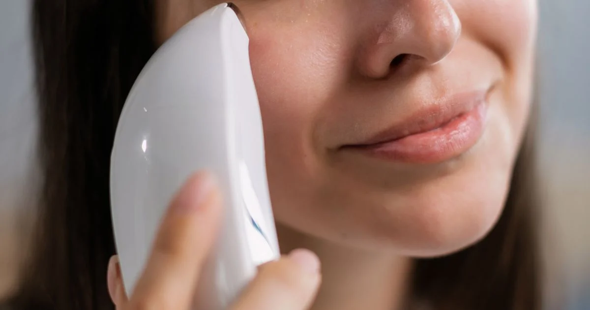 A handheld at-home facial device held along the jawline, the purchase behind the question is microcurrent facial device worth it