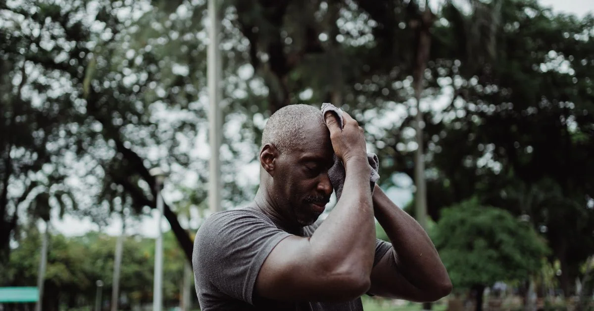A man wiping sweat with a towel after an outdoor run, the heat and moisture behind asking is running headphones worth it