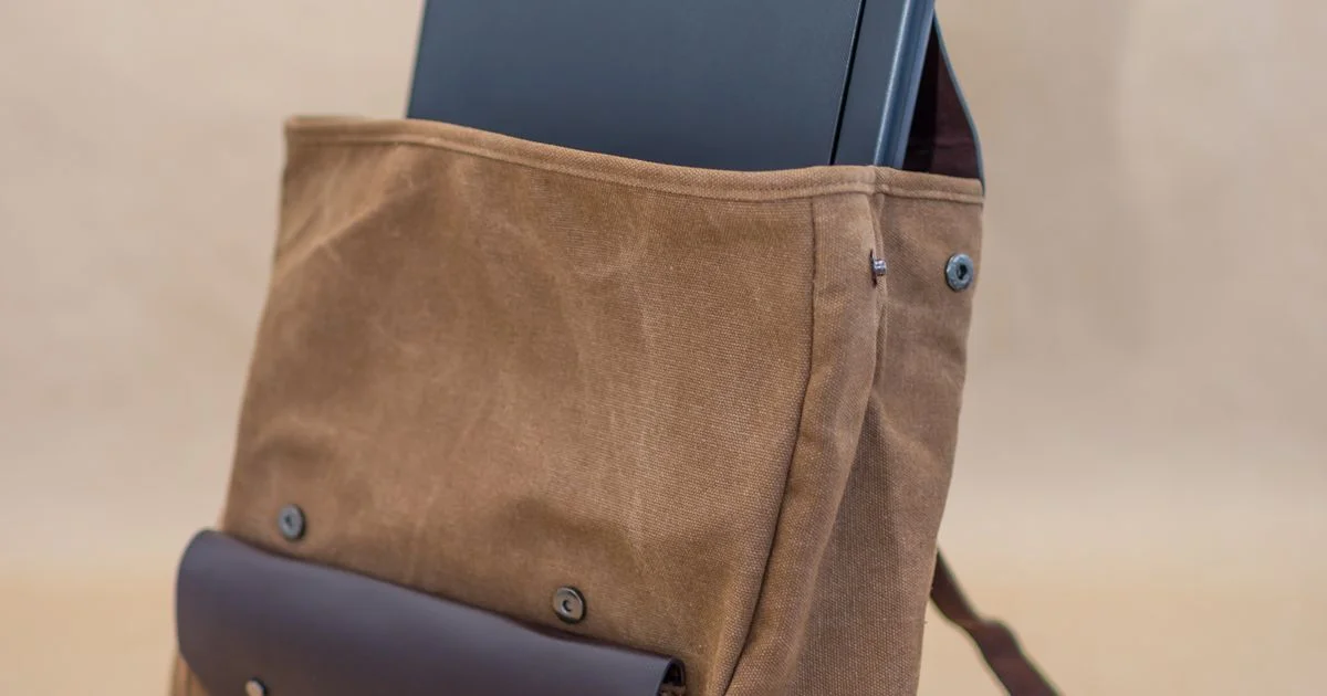 A canvas laptop backpack with a laptop sliding into the outer pocket, the bag behind the question is smart backpack worth it