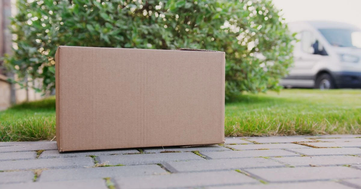 A plain unmarked cardboard parcel on a path outside a house, the way affordable Amazon gadgets arrive with nothing on the box about what is inside