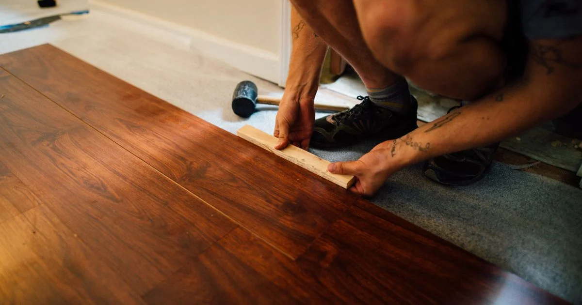 An installer kneeling to tap a plank into place, the labor line that affordable laminate flooring is priced around