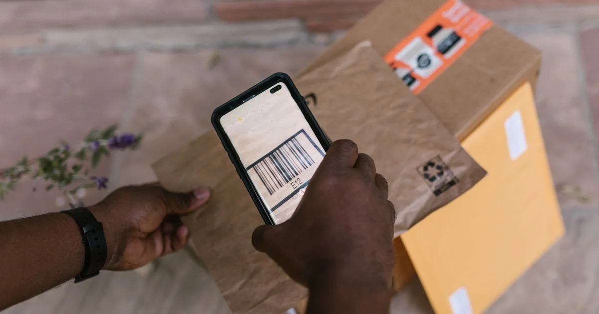 A phone held over a parcel with the striped label showing on screen, the job a barcode scanner app under $5/month is bought to do