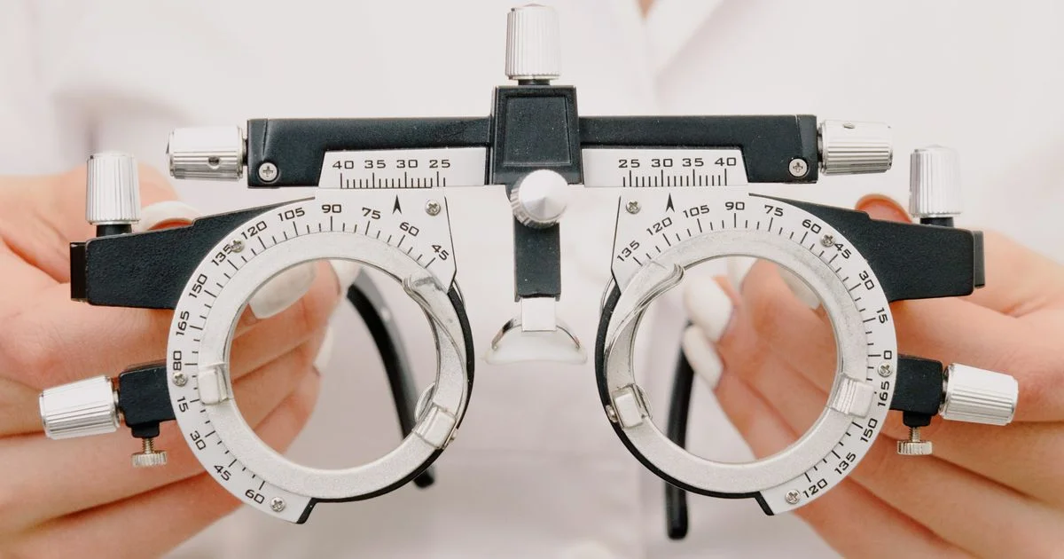 An optometrist holding a trial frame marked with axis and pupil distance scales, the measurements a prescription insert for cheap smart AR glasses under $300 needs