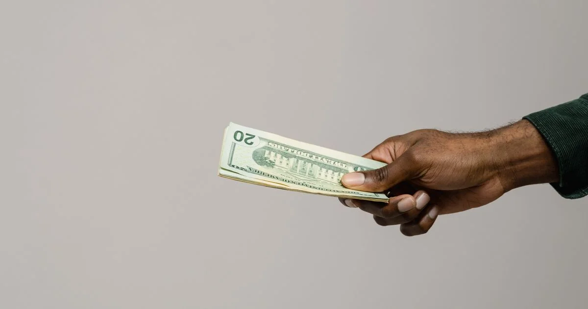 A hand offering a stack of US twenty dollar bills, the cash side of is video game trade in worth it