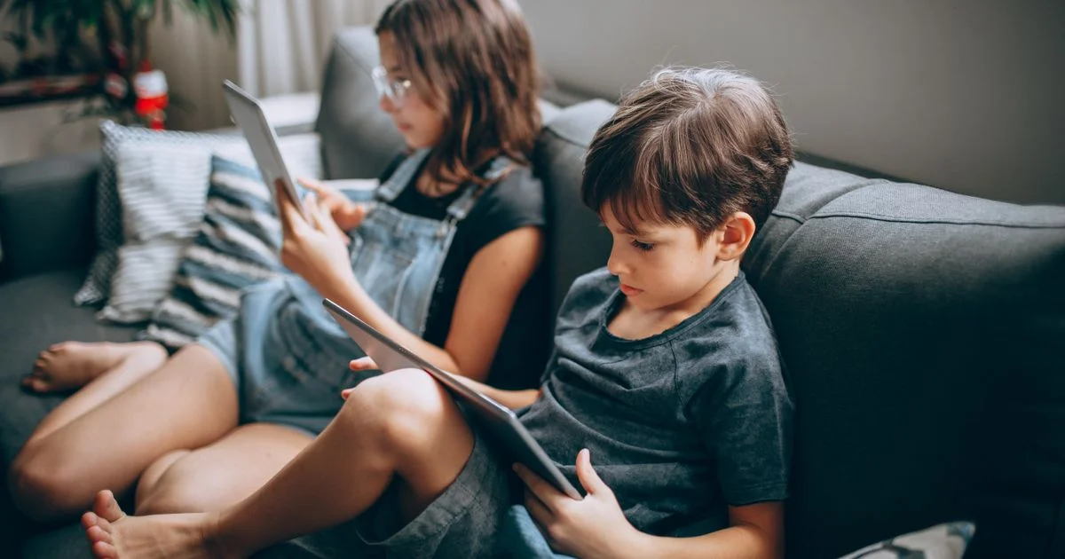 Two children on a sofa each using their own tablet, the device count that decides what multi device antivirus under $60 really costs